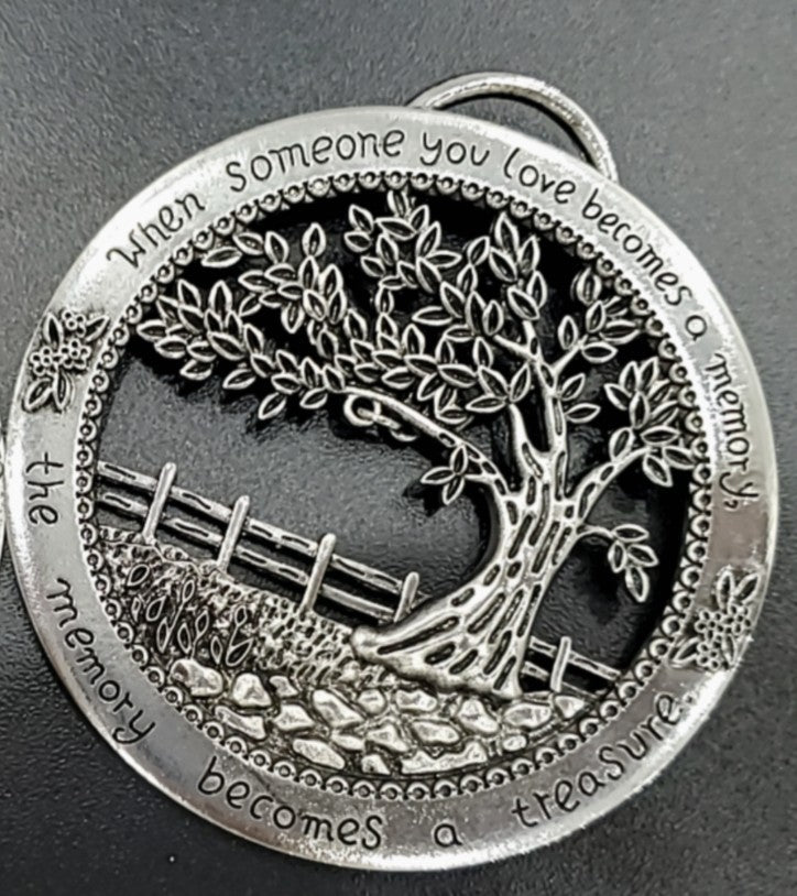 Silver tree ornament with engraved text on a dark background