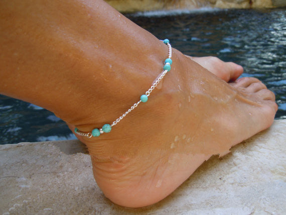 Ankle bracelet with turquoise beads on a foot by a pool
