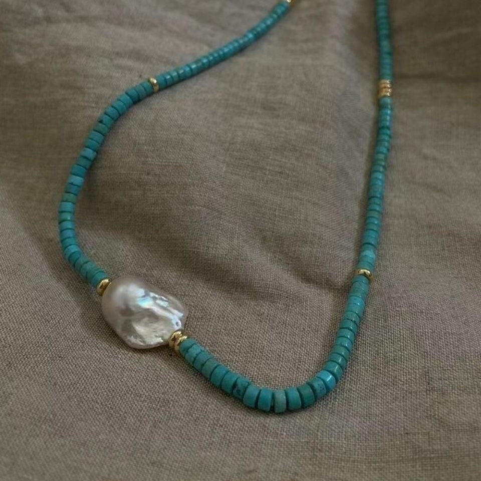 Turquoise beaded necklace with a large pearl pendant on a textured fabric background