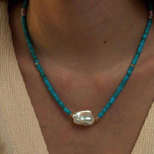 Turquoise beaded necklace with a large pearl pendant on a person wearing a beige top.