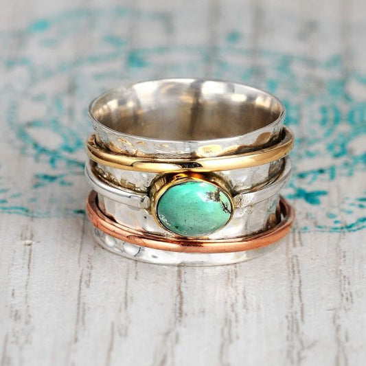 Stack of silver, gold, and copper rings with a turquoise stone on a textured surface.