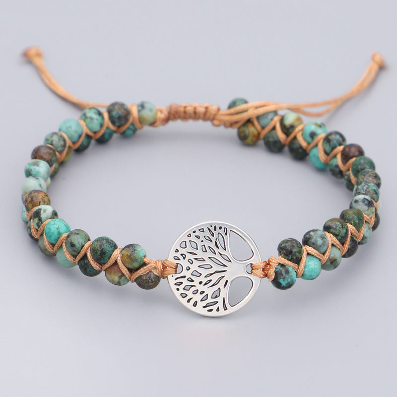 Bracelet with turquoise beads and a silver tree-of-life charm on a light gray background
