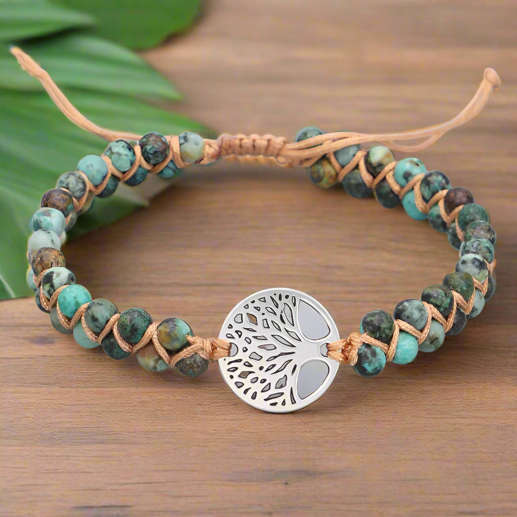 Bracelet with turquoise beads and a silver tree-of-life charm on a light gray background