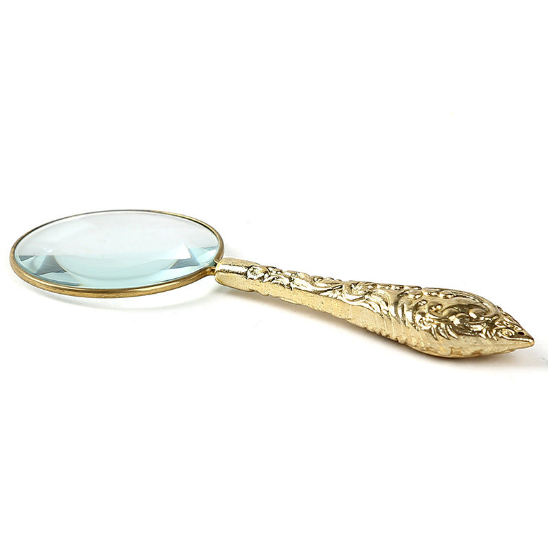 Gold magnifying glass with intricate design on a white background
