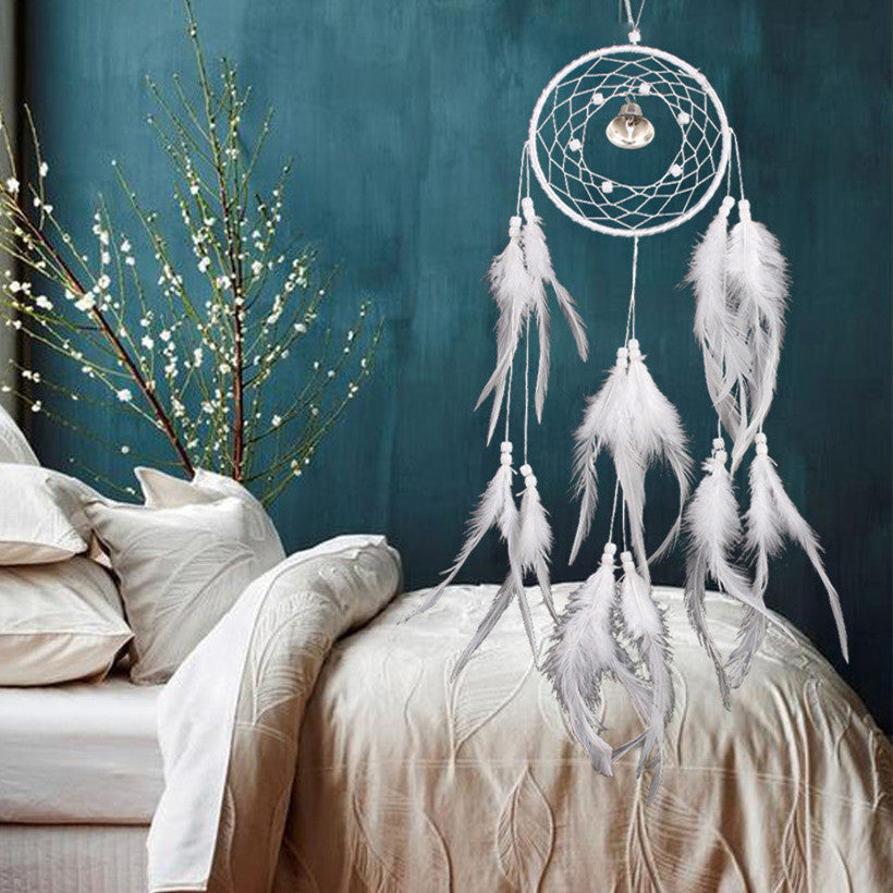 White dreamcatcher with feathers hanging above a bed against a teal wall.