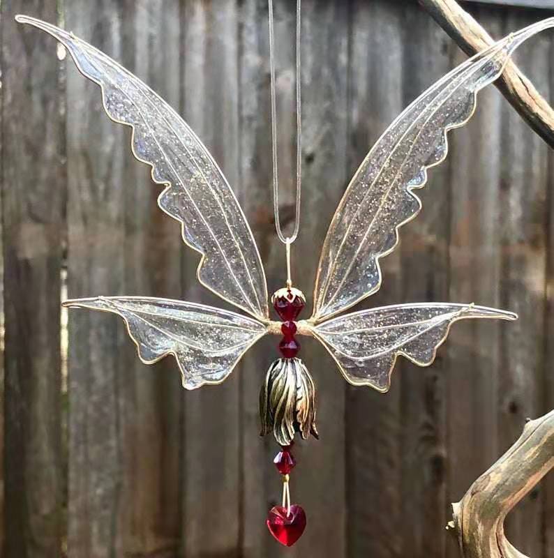 Decorative fairy figurine with transparent wings and red heart-shaped pendant against a wooden background