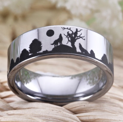 Silver ring with engraved design of a wolf howling at the moon and trees on a natural background