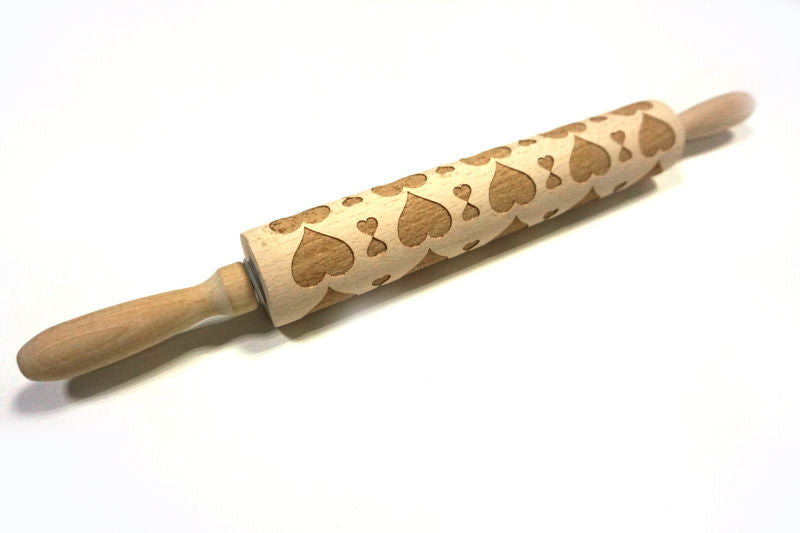 Wooden rolling pin with embossed heart patterns on a white background