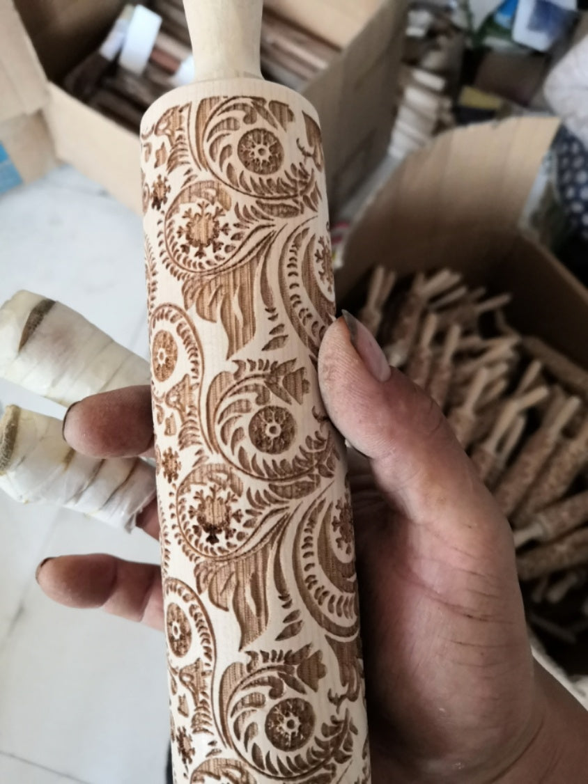 Decorative rolling pin with intricate patterns held by a hand, with more rolling pins in the background.
