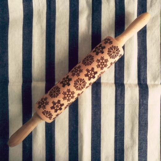 Wooden rolling pin with snowflake pattern on a striped fabric background