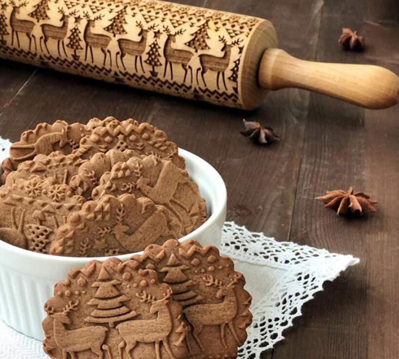 Wooden rolling pin with embossed designs next to cookies on a wooden surface