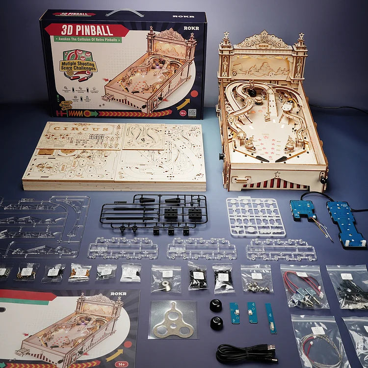 Wooden 3D pinball machine kit with components and packaging on a blue surface