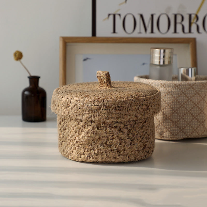 Woven storage basket with a lid on a striped surface, with a blurred 'TOMORROW' poster in the background.