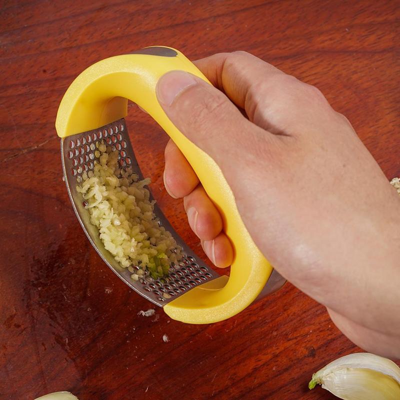 Hand holding a yellow garlic press with minced garlic on a wooden surface
