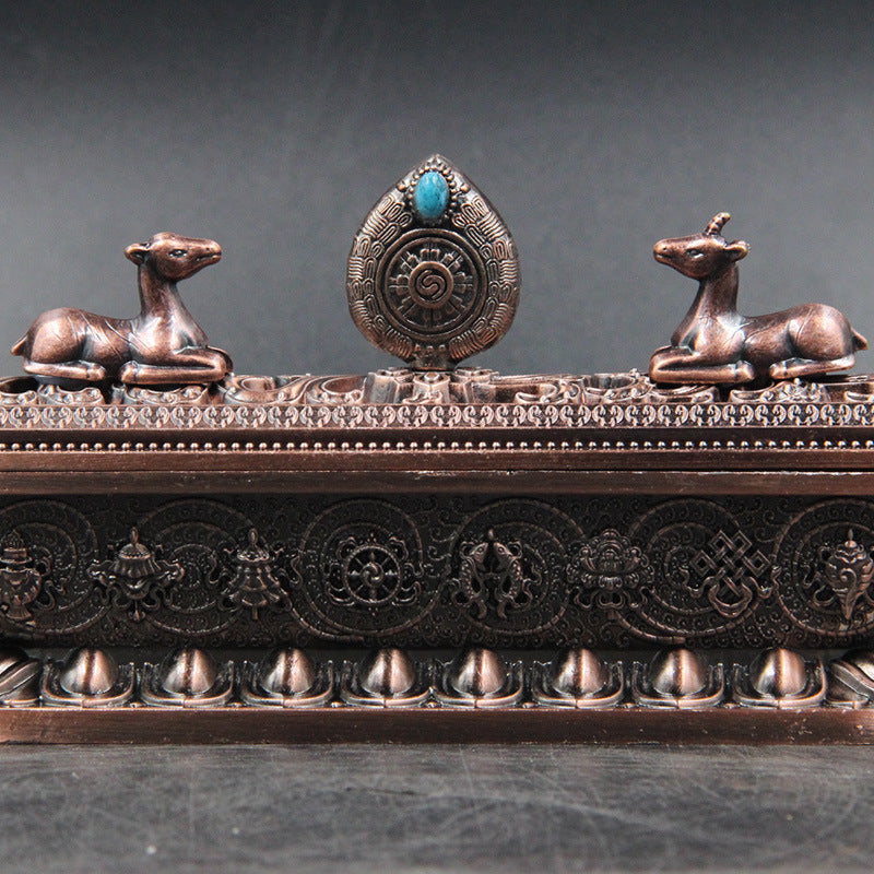 Decorative object with two bronze deer figures and a central turquoise stone on a dark background
