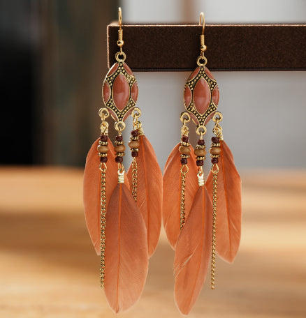 Pair of earrings with pink feathers and gold accents on a wooden surface. From Nested Wisdom