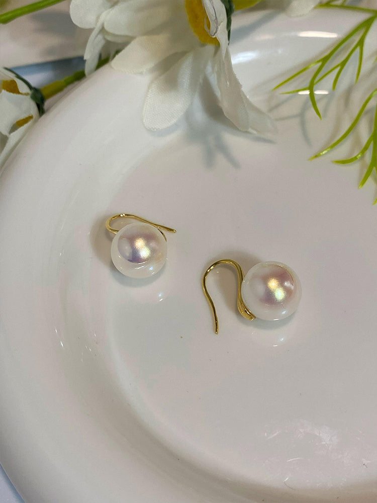 Pearl earrings on a white dish with flowers in the background
