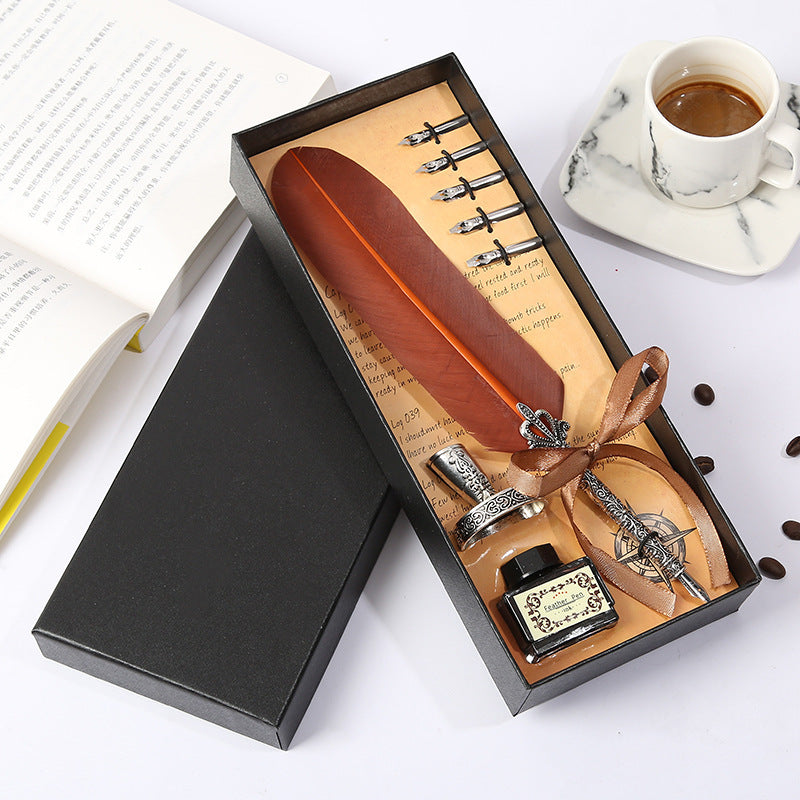 Feather quill pen set with ink bottle in a gift box on a white surface with coffee and notebook.