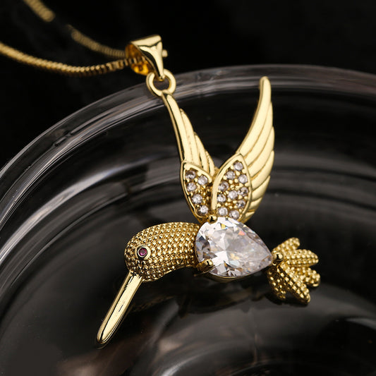 Gold hummingbird-shaped pendant with a clear gemstone on a dark background