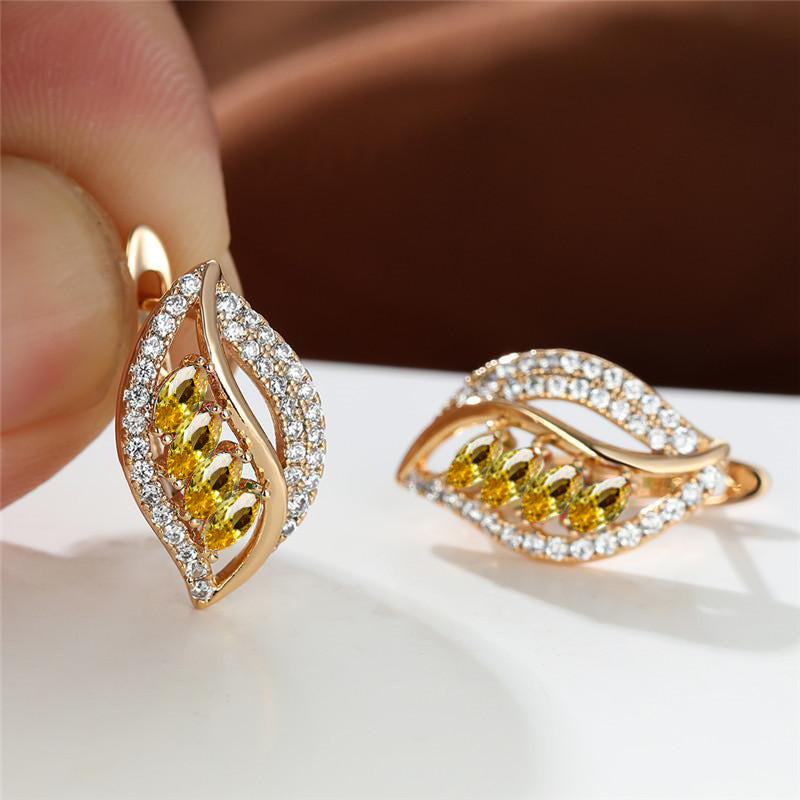 Gold earrings with yellow gemstones held by a hand on a white surface.