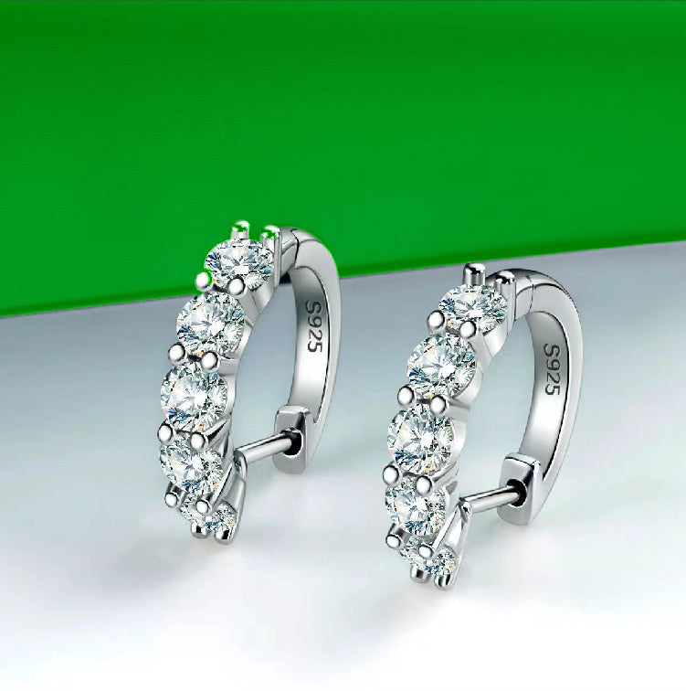 Silver hoop earrings with clear gemstones on a white surface with a green background