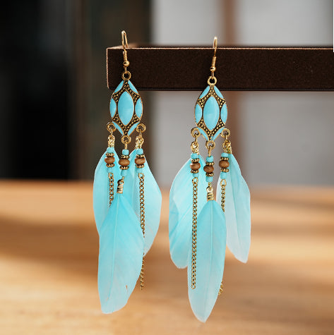 Turquoise feather earrings with gold accents on a wooden surface from Nested Wisdom