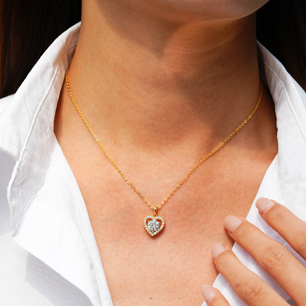 Gold heart-shaped necklace with a diamond pendant on a person wearing a white shirt.
