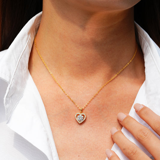Gold heart-shaped necklace with a diamond pendant on a person wearing a white shirt.