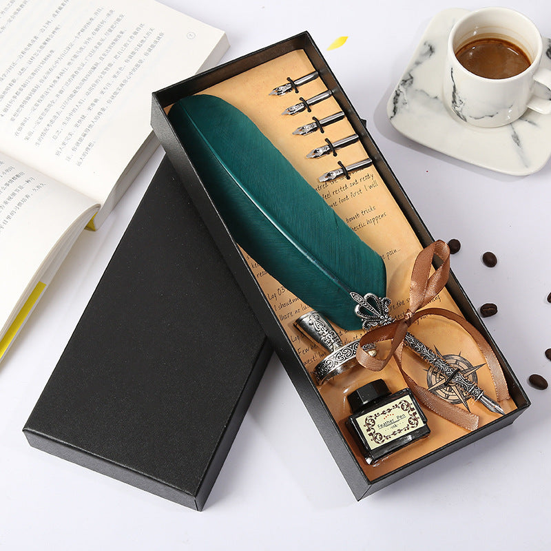 Green feather quill pen set with ink bottle and nibs in a decorative box on a white surface.