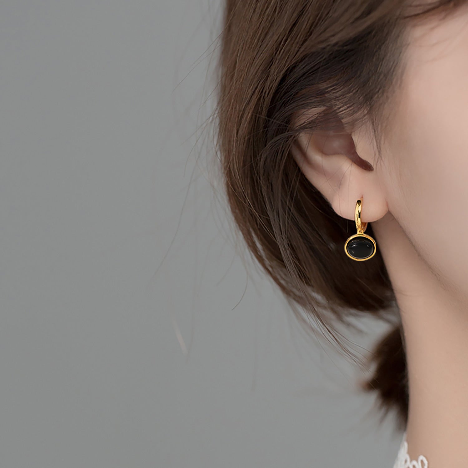 Close-up of an ear wearing a gold earring with a black stone on a neutral background