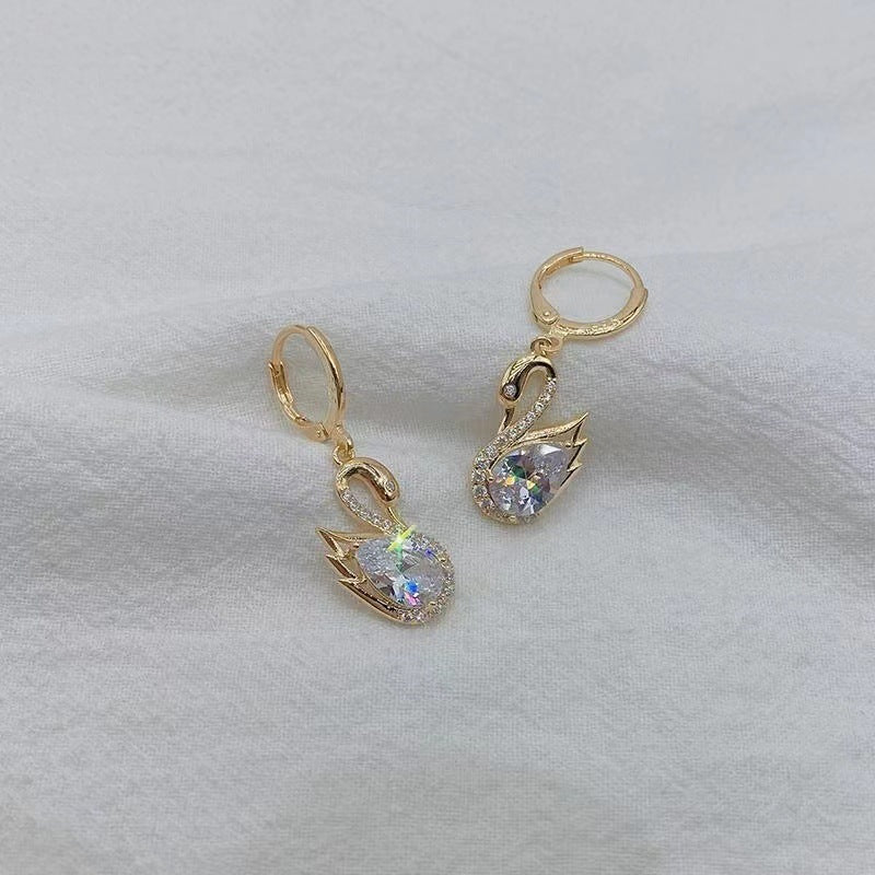 Gold Swan-shaped earrings with gemstones on a light gray background