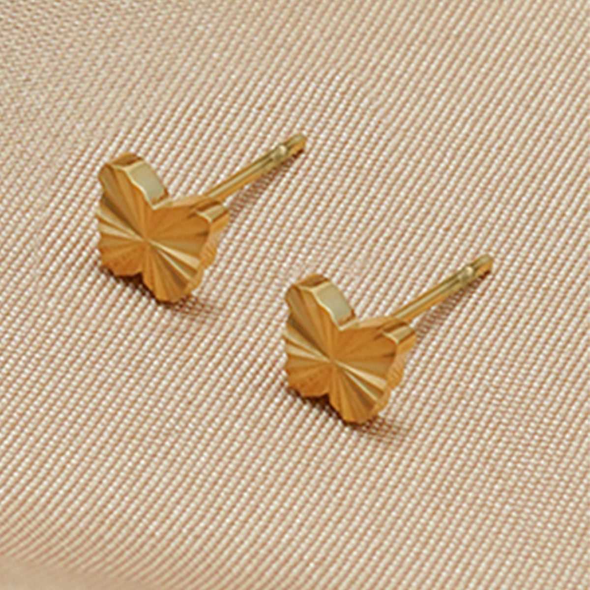Pair of gold leaf-shaped earrings on a beige fabric background