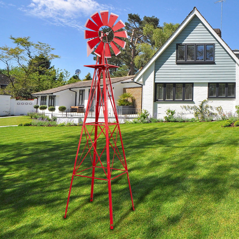 Red windmill on a grassy lawn in front of a house