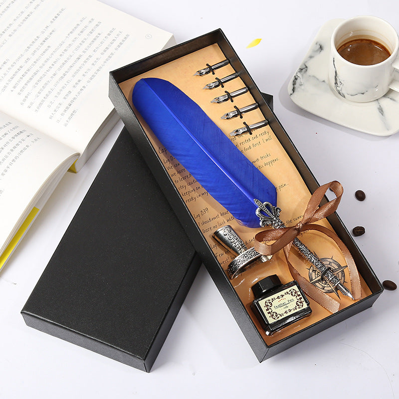 Fountain pen set with blue feather, ink bottle, and nibs in a black box on a white surface.
