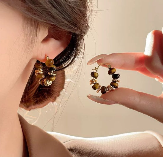 Close-up of a person wearing a gold and green beaded earring with another hand holding a similar earring from nested wisdom