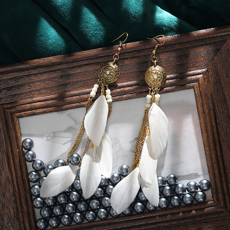 Pair of earrings with white feathers and gold accents displayed in a wooden frame.