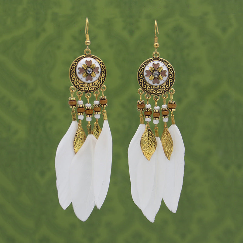 Pair of gold and white feathered earrings on a green patterned background