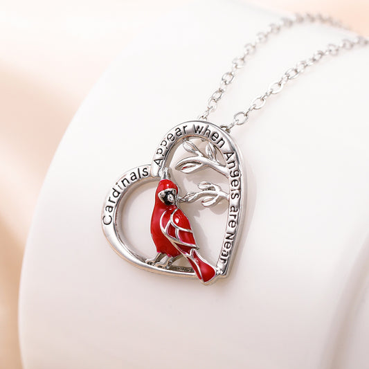 Heart-shaped necklace with a red bird pendant and engraved text on a white surface