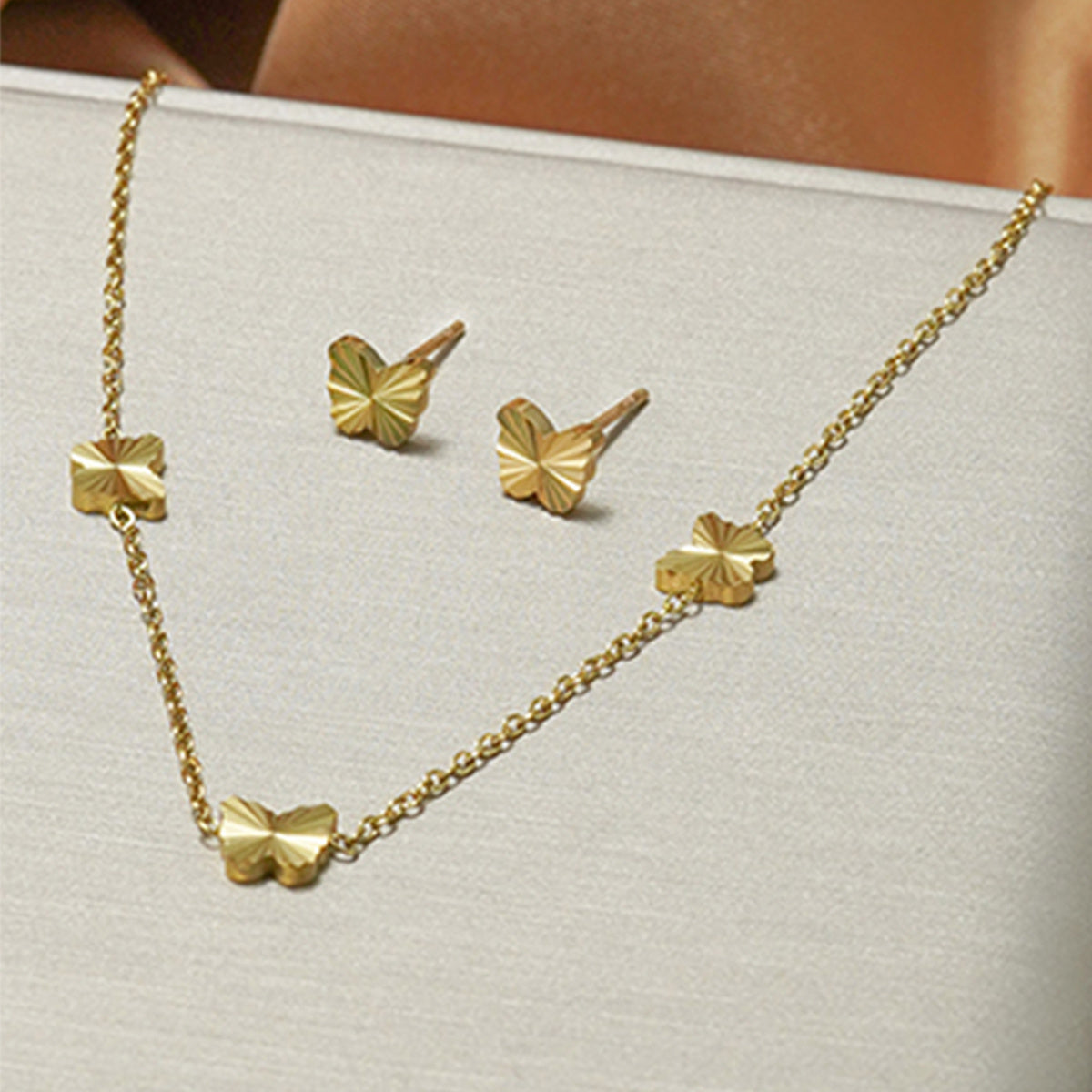 Gold necklace and earrings set on a light gray surface