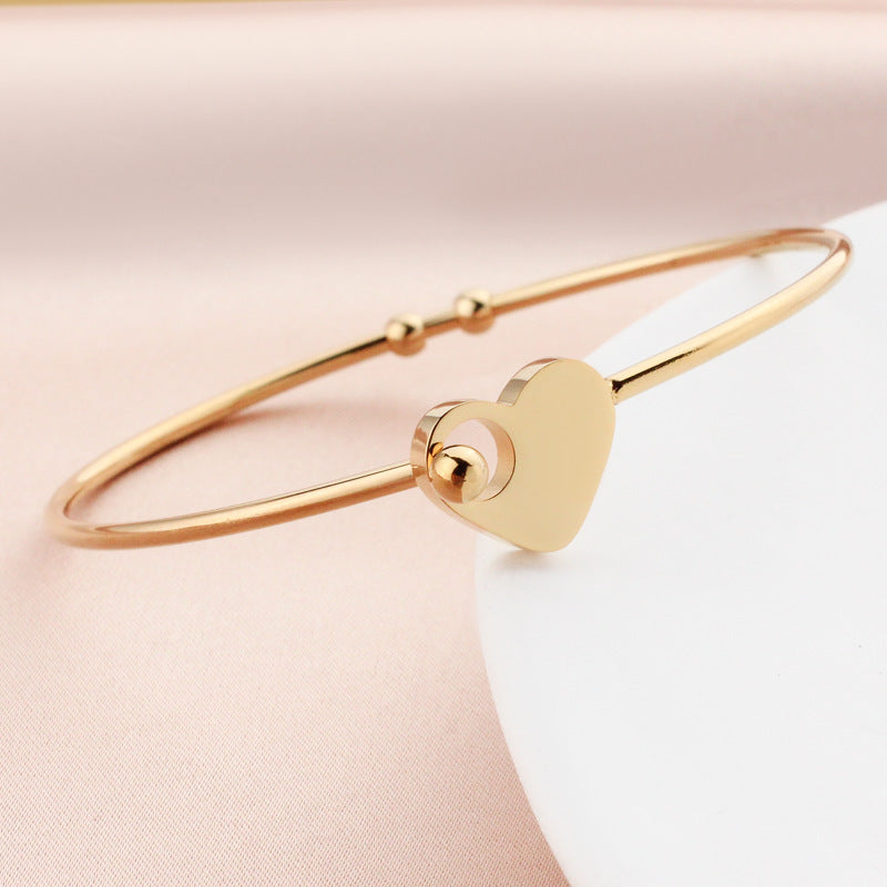 Gold bracelet with a heart-shaped clasp on a light pink background
