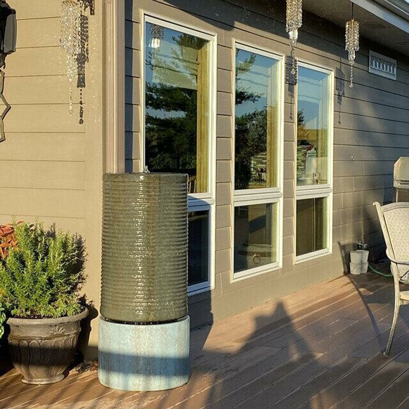 Decorative cylindrical planter on a wooden deck with a house in the background