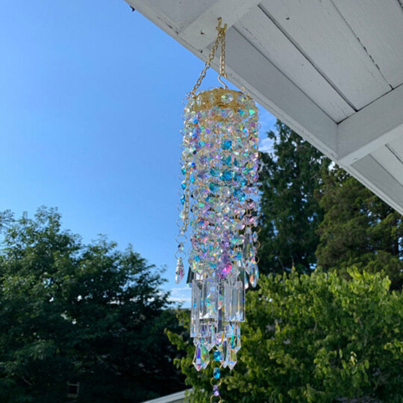 Decorative crystal chandelier wind chime hanging from a roof with trees and blue sky in the background