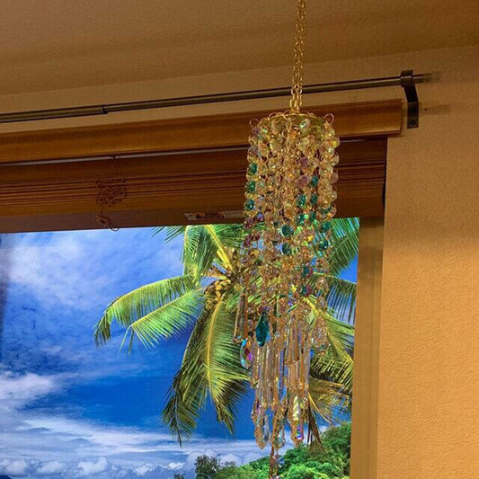 Decorative chandelier style crystal wind chimes hanging in front of a window with a tropical view outside.