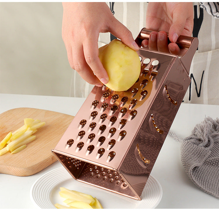 Rose gold box grater being used to shred an apple on a white surface.