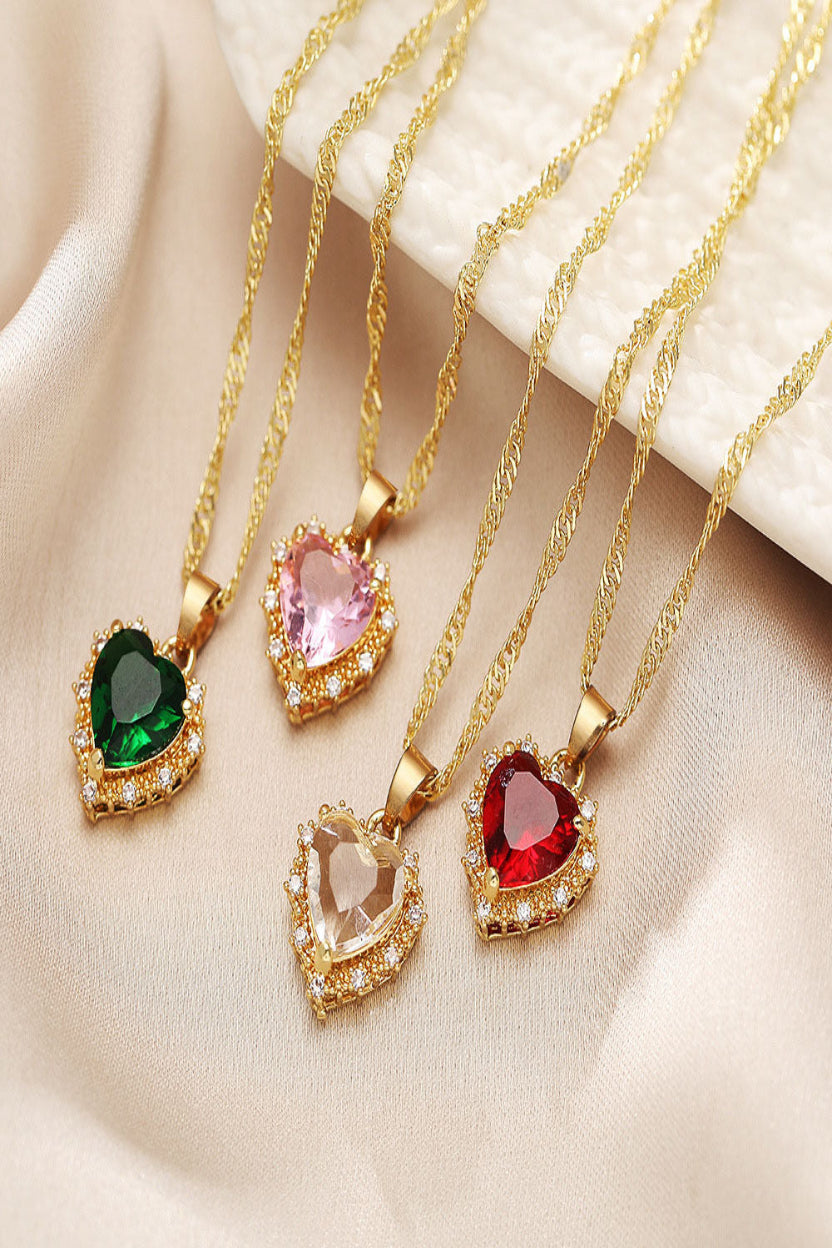 Four gold necklaces with heart-shaped gemstones on a beige fabric background