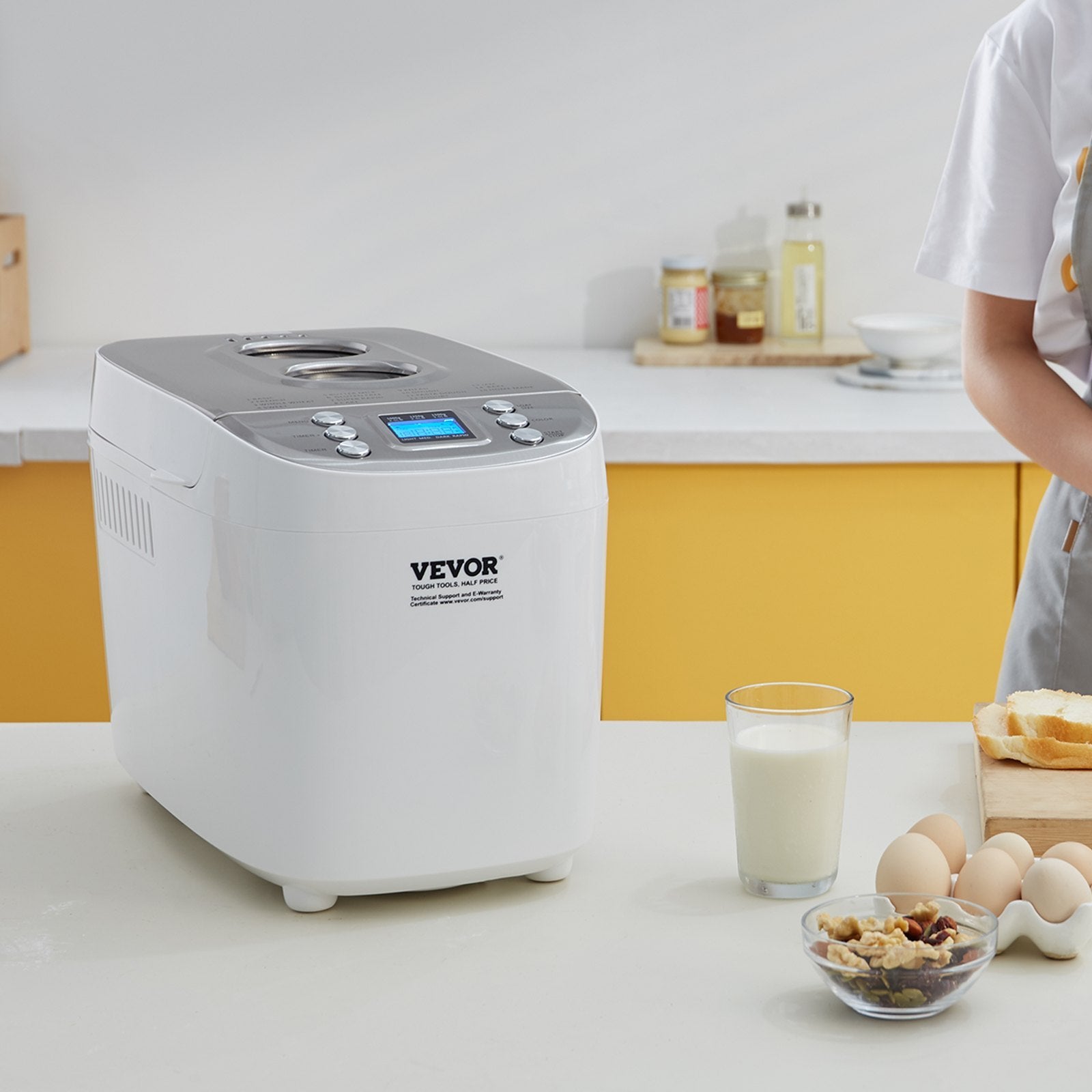 Vevor bread maker on a kitchen counter with a glass of milk, bowl of nuts, and eggs.