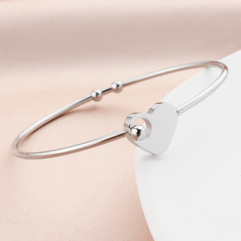 Silver bracelet with a heart-shaped clasp on a soft pink background