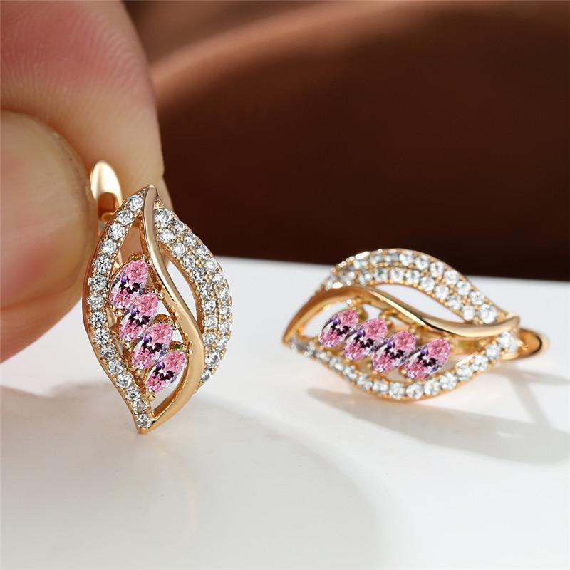 Gold earrings with pink gemstones held by a hand on a white surface.
