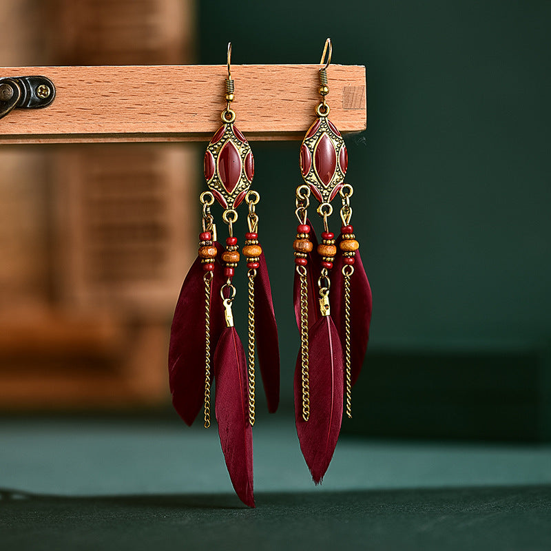 Red feather earrings with gold accents on a wooden stand against a dark green background from Nested Wisdom