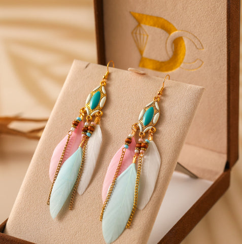 Colorful feather-shaped earrings on a beige card with a brand logo in the background from Nested Wisdom